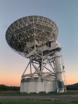 A large satellite dish stands tall against a colorful sunset, symbolizing advanced technology.