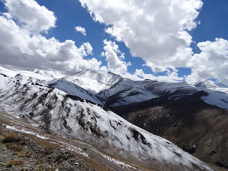 Serene snow-covered mountains under a clear blue sky with fluffy white clouds.
